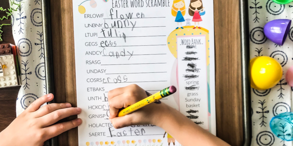 child writing with a pencil on easter word scramble sheet