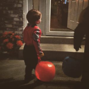 Child holding a plastic pumpkin standing at front door