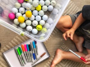 child holding a marker next to golf balls